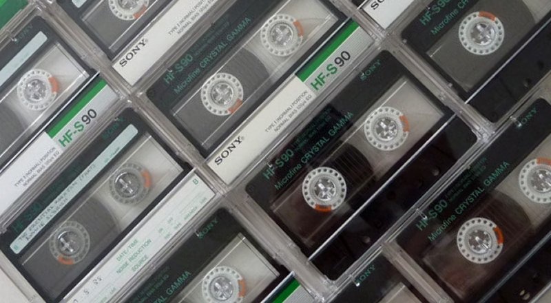 An array of Audio Cassette Tapes are shown side by side in te photo. They are mainly Sony C90 and C60 with their reels rewound, and have green and silver labels.