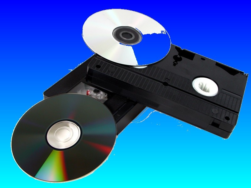 A VHS video tape shown together with some DVD disks ready for transfer of the footage between the vhs cassette and the dvd.